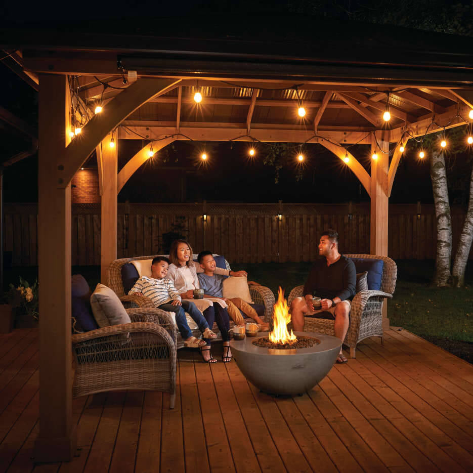 Family gathered around a fire pit under a wooden pergola at night.