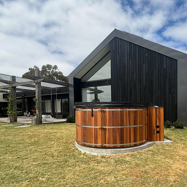Wooden hot tub in front of a modern house with a clear sky.